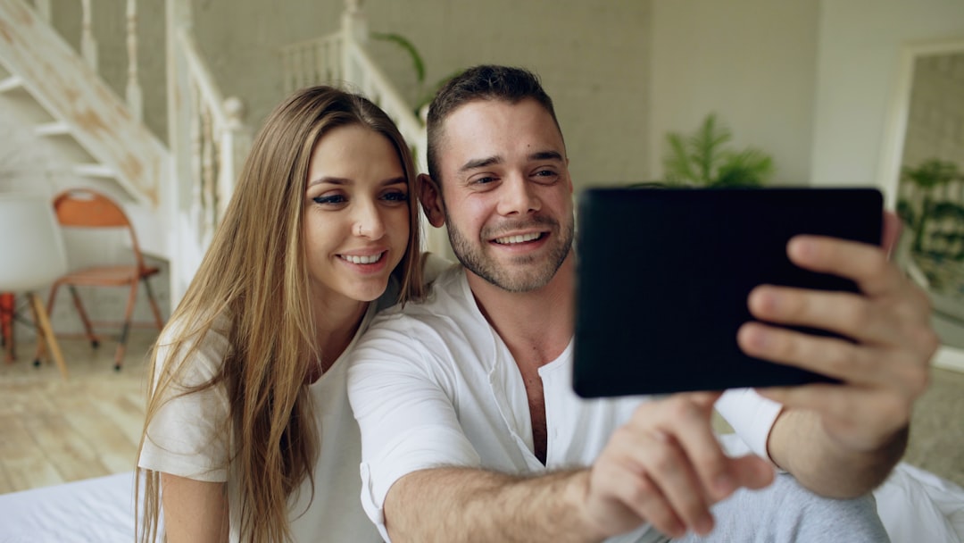 Young cute and loving couple having video chat holding tablet computer camera and chatting to friends sitting in bed at home