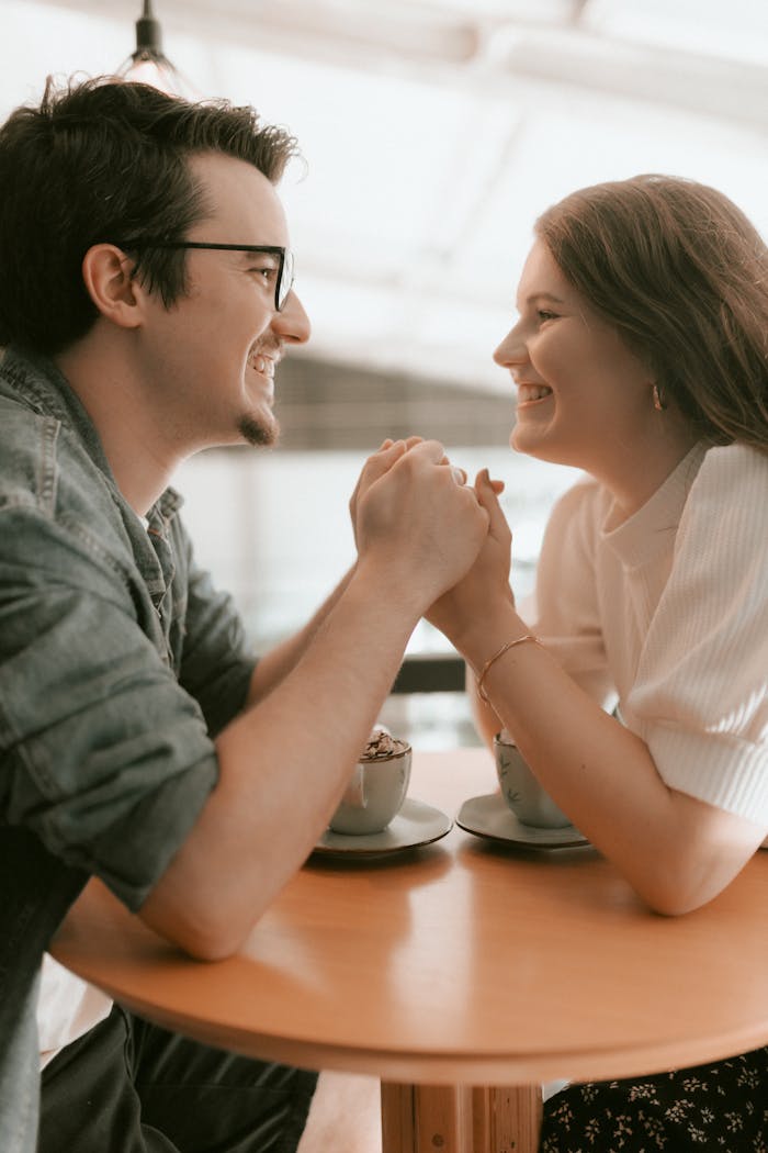 Couple smiling and holding hands at a cozy cafe, enjoying their coffee date.